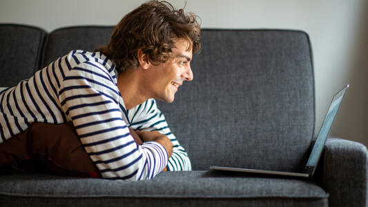 Jeune homme regardant son ordinateur sur son canapé